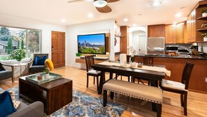 Una sala de estar moderna con un televisor grande, muebles de madera y un comedor con una cocina al fondo.