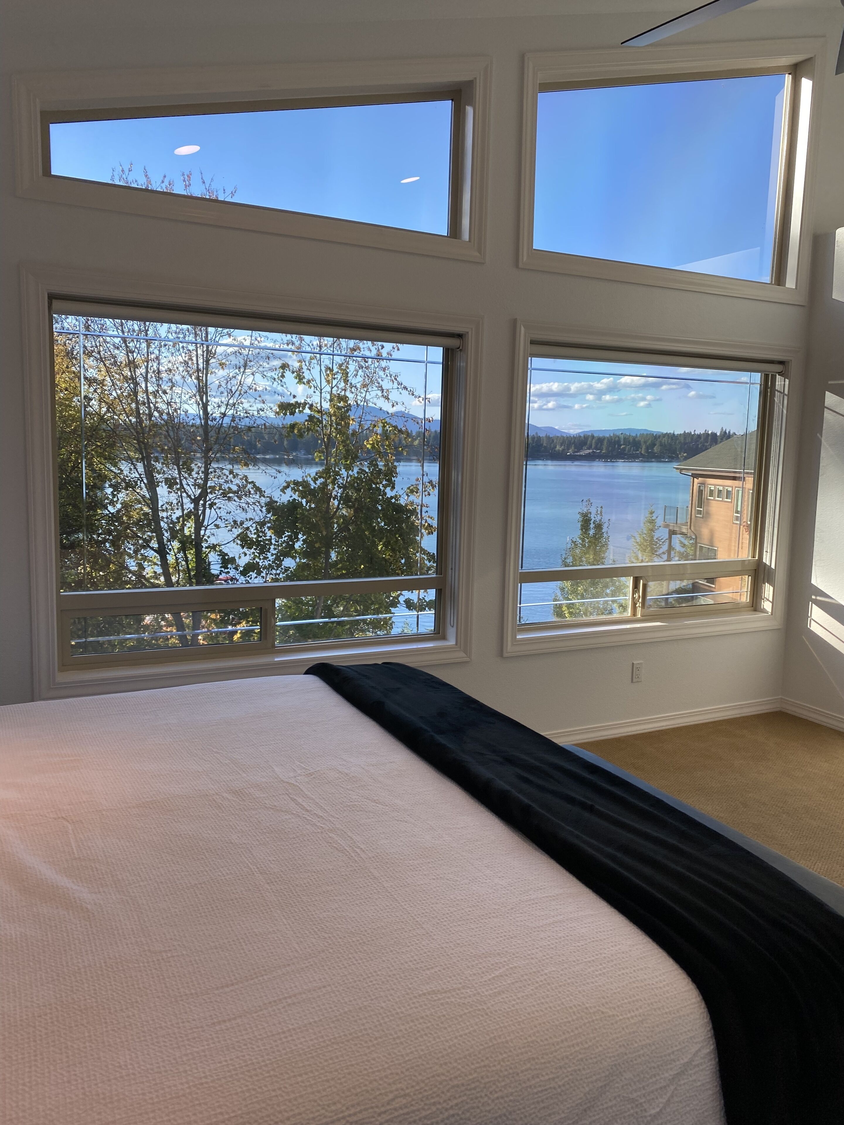 Ett sovrum med en stor säng, flera fönster och utsikt över en sjö och berg.