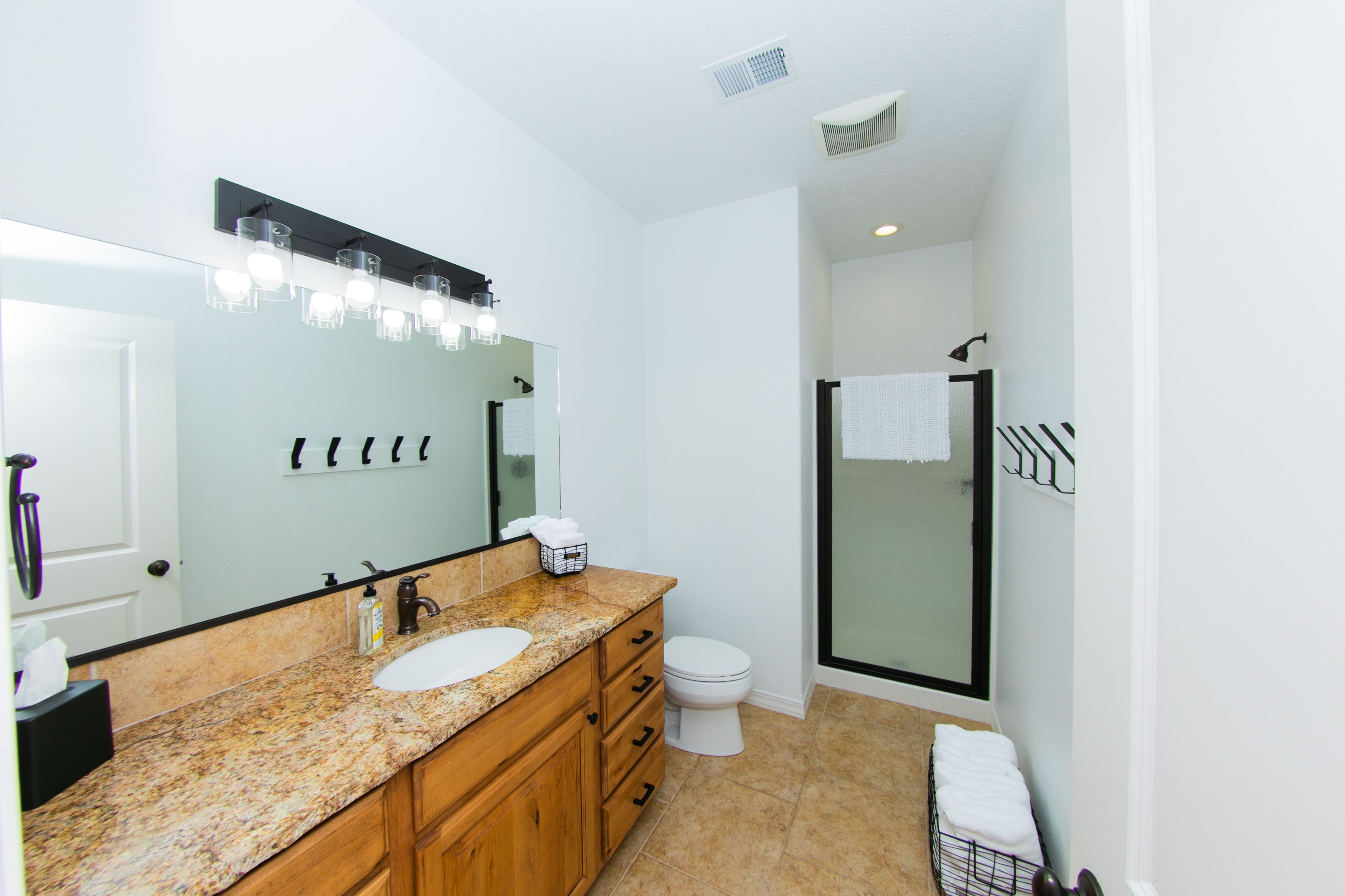A bathroom with a double sink vanity, a toilet, a glass shower enclosure, and a large mirror with overhead lighting.