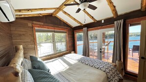 A bedroom with a large bed, wooden ceiling beams, a ceiling fan, and a view of a lake through large windows. - 2-bedroom vacation home near Mark Twain National Forest (Potosi)
