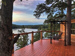 A wooden deck with a swing chair overlooking a lake.