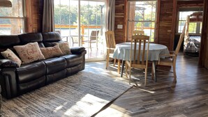 A cozy living room with a leather sofa, wooden dining table, and chairs. Large windows offer a view of the outdoors. - 2-bedroom vacation home near Mark Twain National Forest (Potosi)