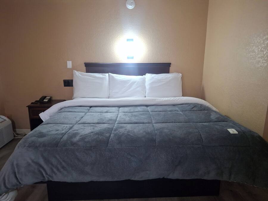 A bed with a grey quilt, white pillows, and a wooden headboard.