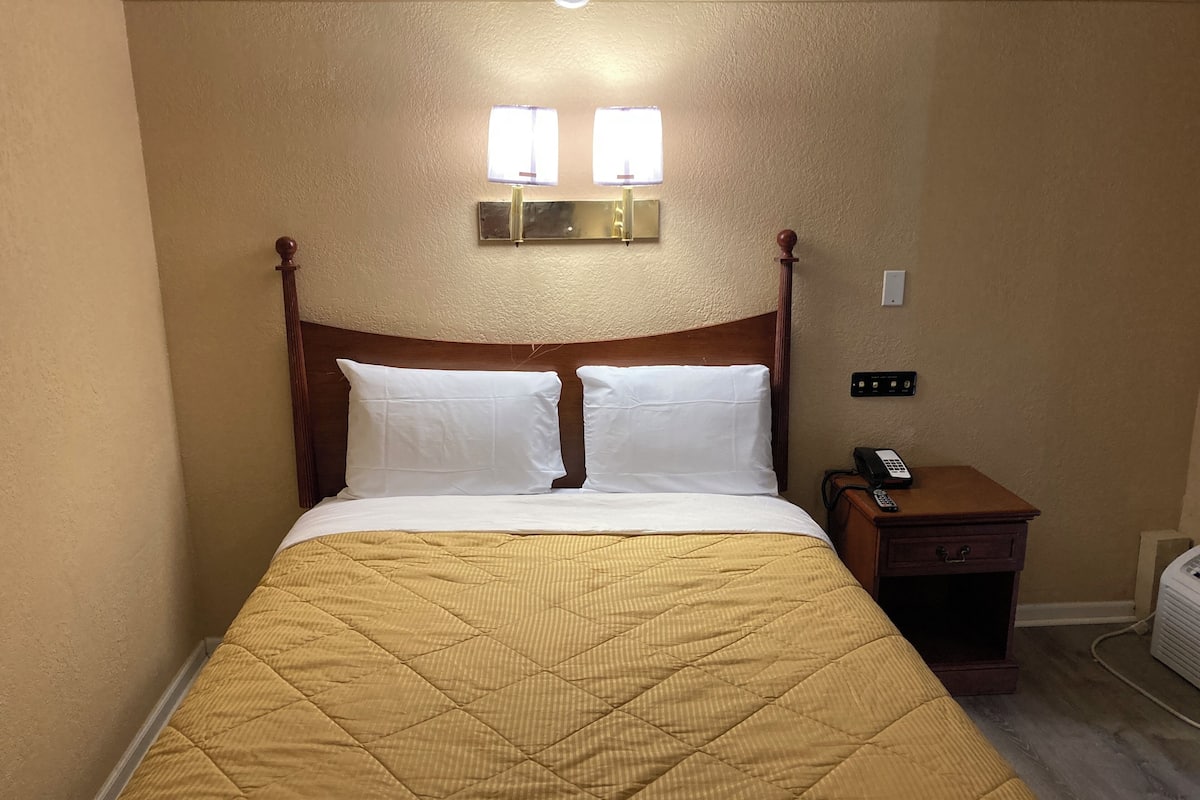 A neatly made bed with a wooden headboard, a bedside table with a phone, and a wall-mounted light fixture.