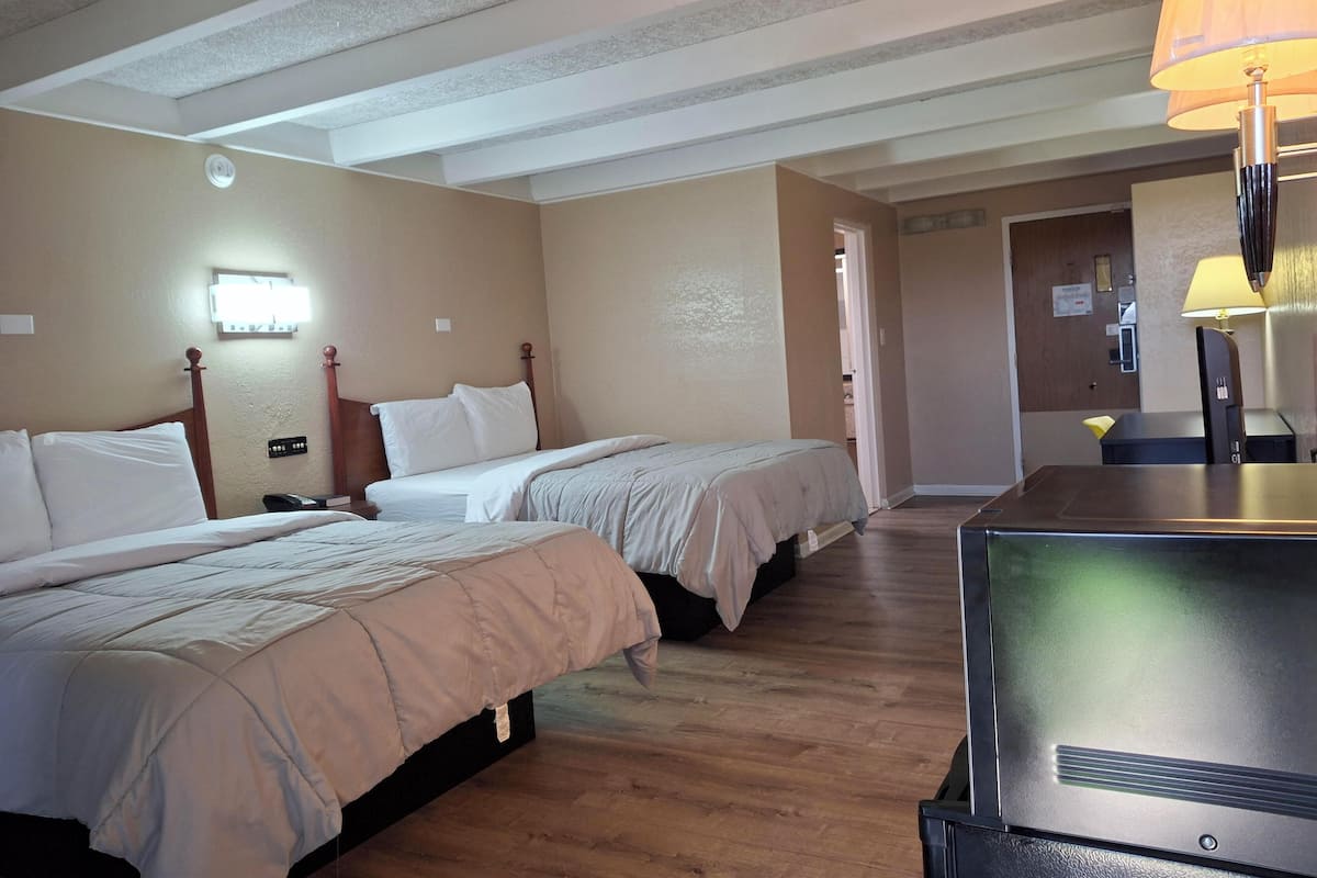 A hotel room with two beds, a desk, a lamp, and a door leading to a bathroom.