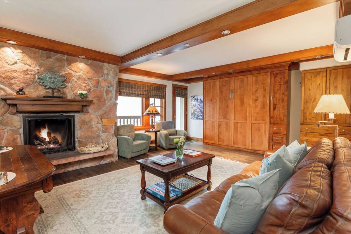 A cozy living room with a stone fireplace, leather sofa, wooden cabinets, and a fireplace mantel.