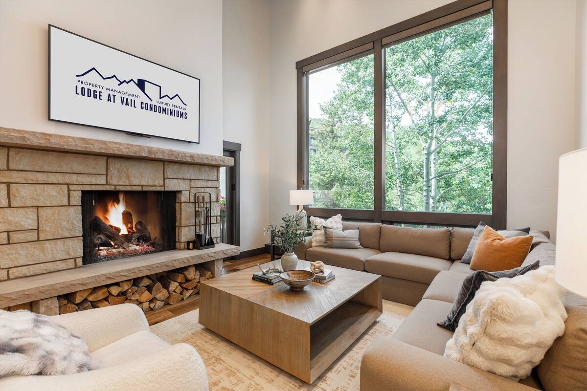 A living room with a fireplace, a sofa, a coffee table, and a large window with a view of trees.