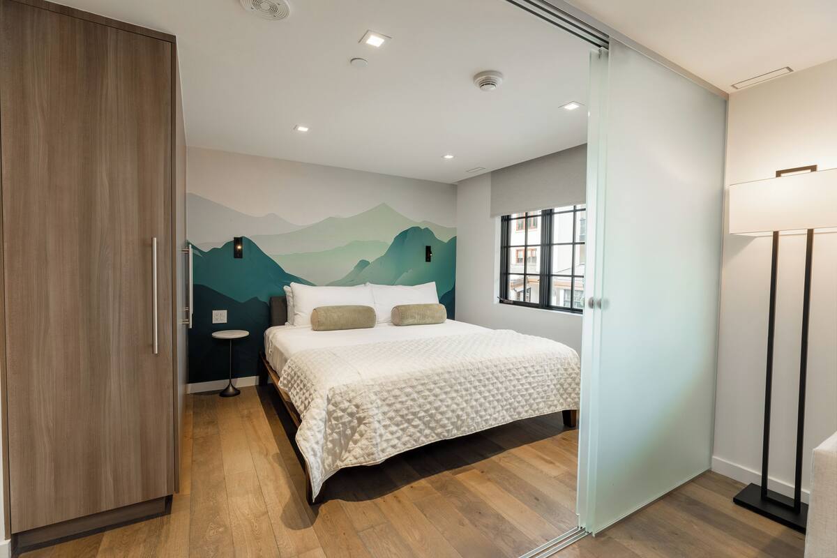 A modern bedroom with a bed, a nightstand, a wall mural, and a window.