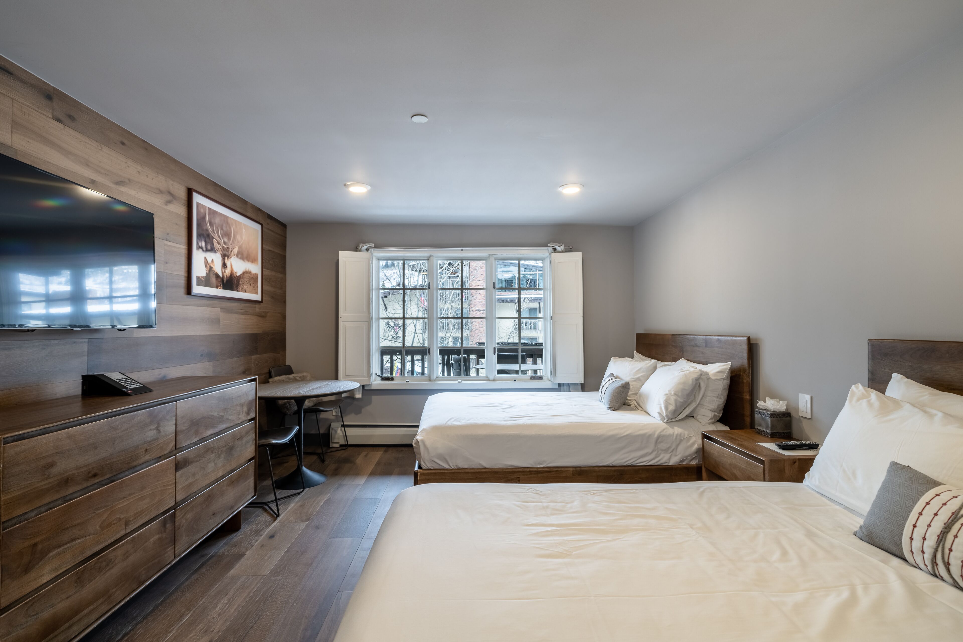 Une chambre d’hôtel moderne, dotée de deux lits, d’une commode en bois, d’un bureau et d’une grande fenêtre donnant sur l’extérieur.