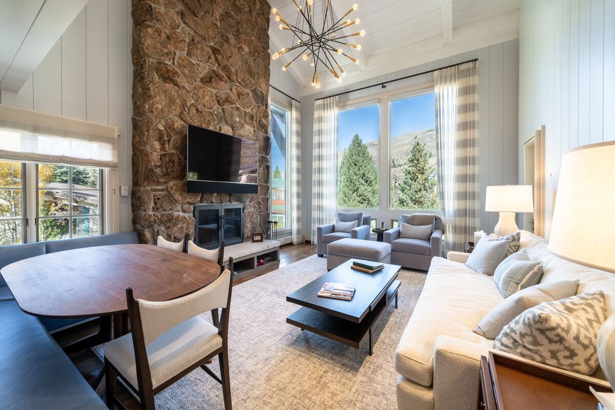 A modern living room with a stone accent wall, a fireplace, a flat-screen TV, a dining table, and a sofa.