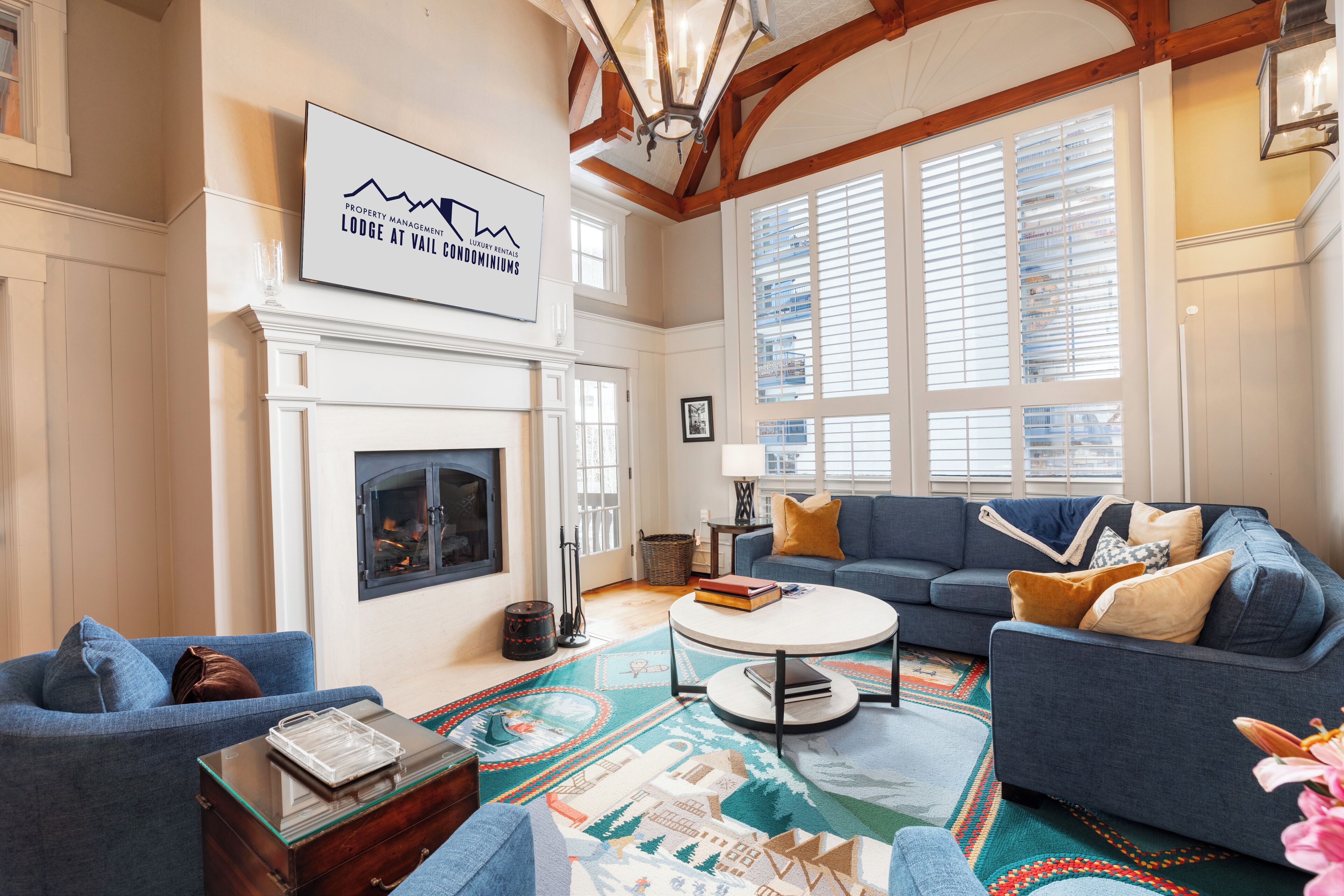 A spacious living room with a fireplace, a blue sofa, a coffee table, and a large window with blinds.