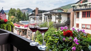 Dos copas de vino en un balcón con vistas a edificios y montañas al fondo.