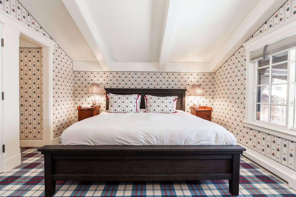 A bedroom with a large bed, two bedside tables, and a window with a view.