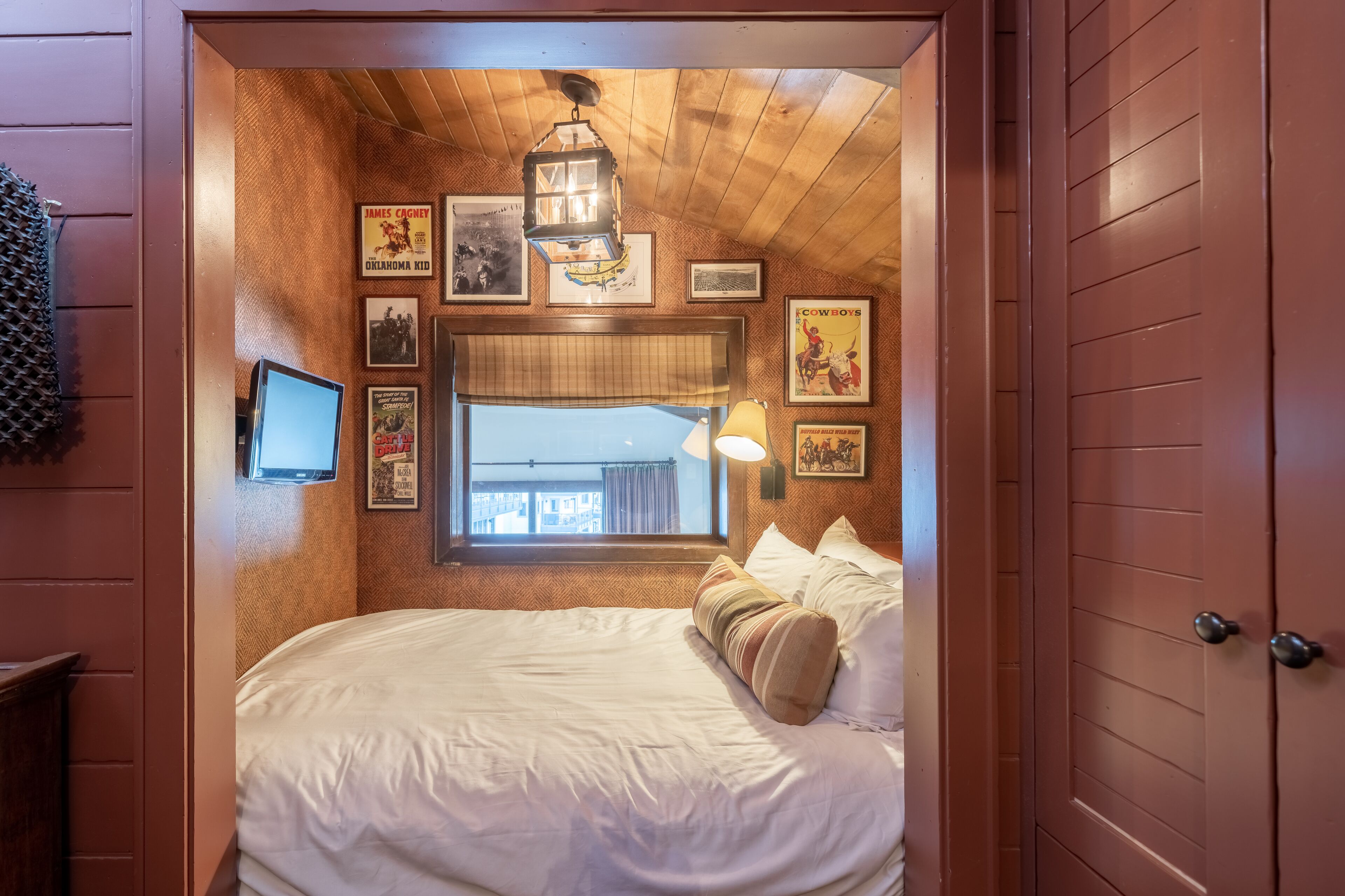A bedroom with a large bed, a window with curtains, and various framed pictures on the wall.
