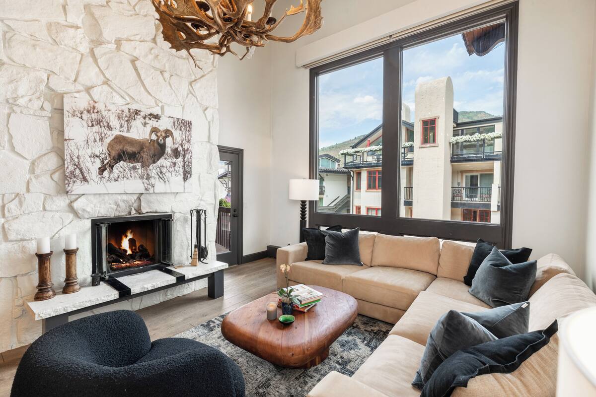 A modern living room with a stone fireplace, a large window with a view of buildings, and a cozy seating area.
