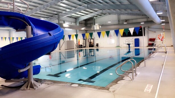En indendørs swimmingpool med en blå rutsjebane, sikkerhedsskilte og en redningsbøje.