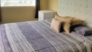 Une chambre à coucher comprenant un lit, une tête de lit, une table de chevet et une fenêtre donnant sur la mer.