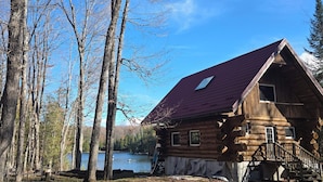 A log cabin with a red roof, surrounded by trees and a lake. - Lake Front Log Cabin (Irondale)