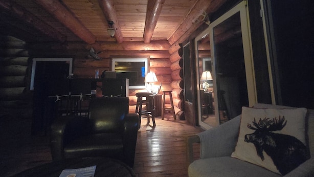 A cozy log cabin interior with a wooden ceiling, a sofa, a coffee table, and a dining area. - Lake Front Log Cabin (Irondale)