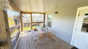 A covered patio with a wooden table and benches, large windows, and a door. - Perfect slice of peace and quiet by<br> (Lake Placid)