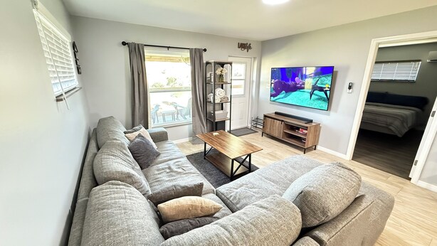 A modern living room with a grey sectional sofa, a wooden coffee table, and a flat-screen TV mounted on the wall. - Perfect slice of peace and quiet by<br> (Lake Placid)