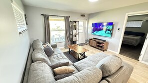 Una sala de estar moderna con un sofá seccional gris, una mesa de centro de madera y un televisor de pantalla plana montado en la pared.