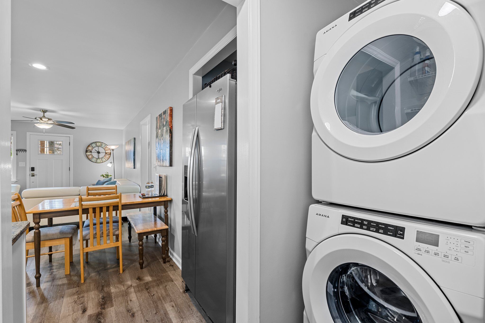 A laundry room with stacked washing machines, a refrigerator, and a dining area with a table and chairs.