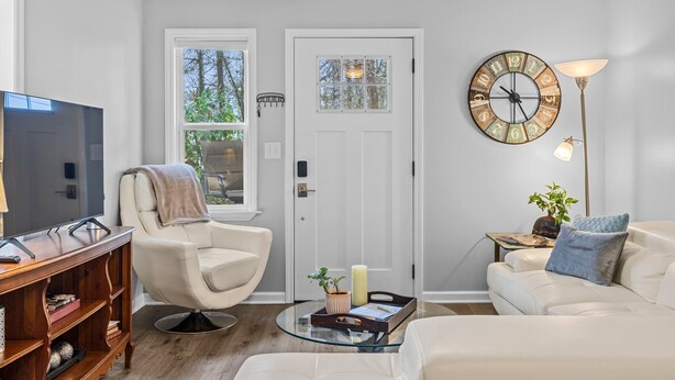 A living room with a television, a white armchair, a sofa, a coffee table, a clock, and a floor lamp. - 1/4 Mile to Ecusta Trail • Firepit • 1G Fiber Wi-Fi • Bamboo Bungalow (Hendersonville)