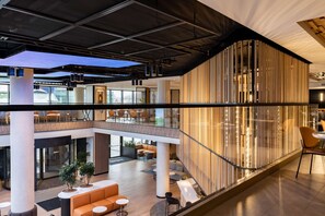 Un intérieur moderne doté d’un atrium central, de plusieurs espaces de détente et d’une balustrade en verre donnant sur l’ensemble de l’espace.