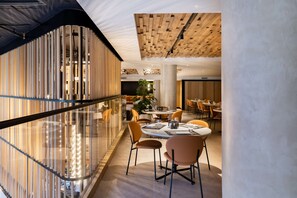 Un espace repas moderne avec des tables et des chaises rondes, une rambarde en verre et un plafond en bois.