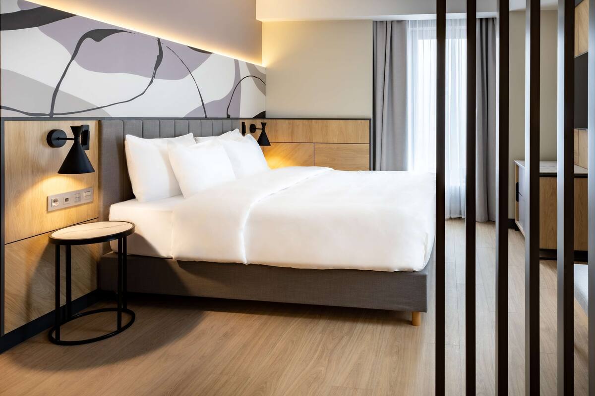 Une chambre d’hôtel moderne, dotée d’un grand lit, de lampes de chevet, d’une petite table ronde et d’un luminaire fixé au mur.