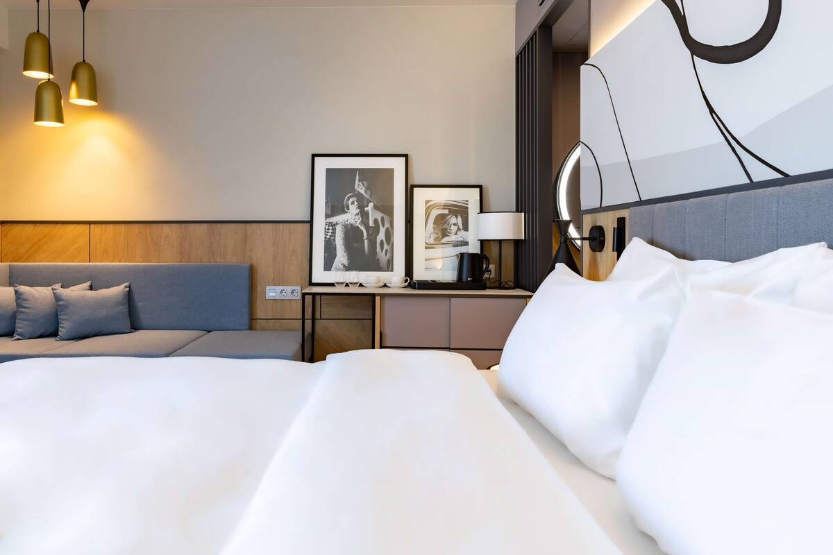 Une chambre d’hôtel avec un grand lit, un petit canapé, une table de chevet avec une lampe et deux tableaux encadrés au mur.