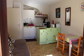 Cocina compacta con comedor, que incluye un armario verde, un microondas y una pequeña mesa con sillas.