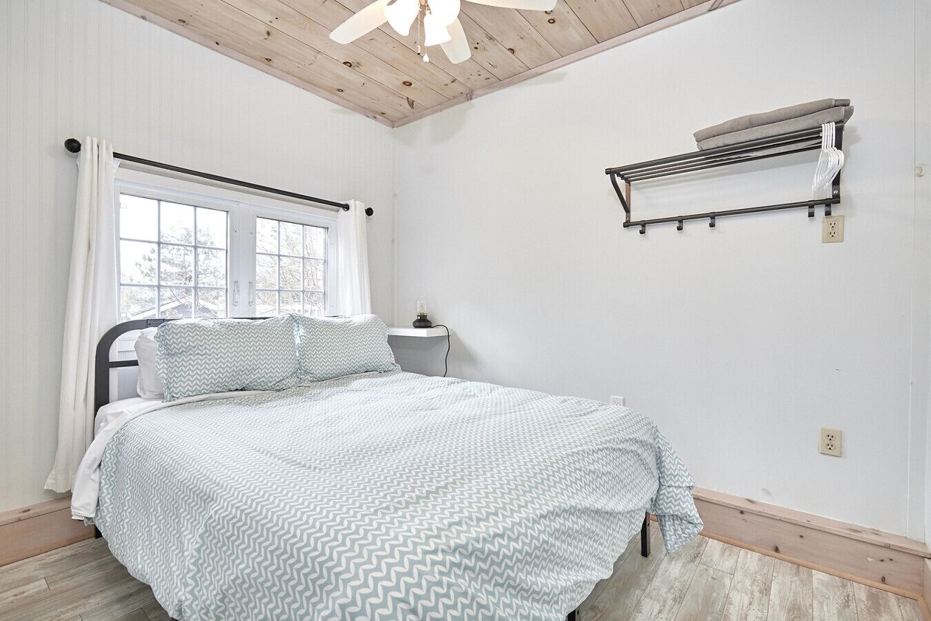 A bedroom with a bed, a window, a ceiling fan, and a wall-mounted air conditioning unit.