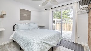 A bedroom with a bed, a ceiling fan, a window with a view of a wooden deck, and a motivational poster on the wall.