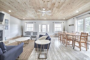 Un vaste salon doté d’un plafond en bois, d’une cheminée, d’un coin repas avec des chaises en bois et de grandes fenêtres.