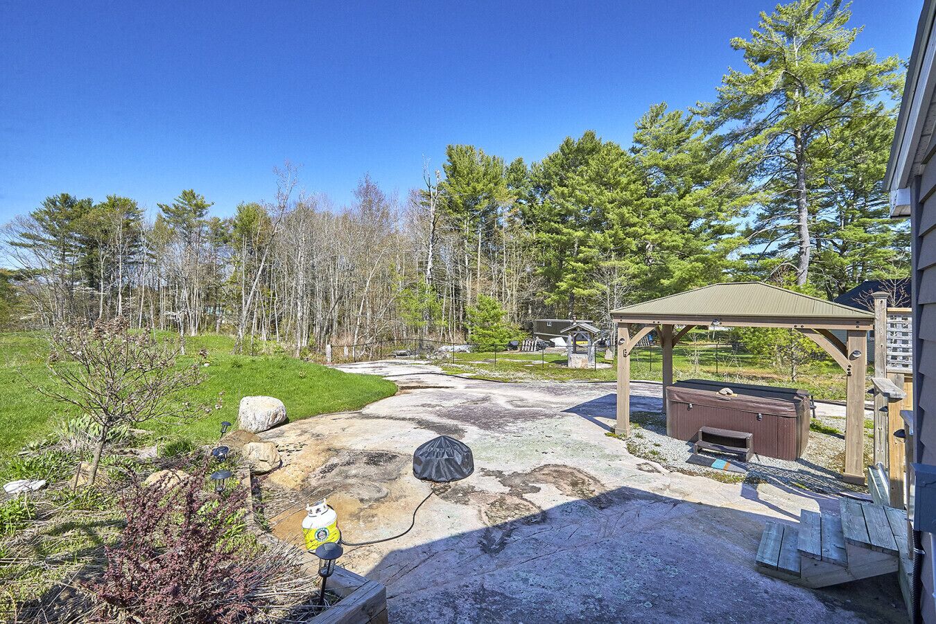 A backyard with a grill, a wooden deck, and a covered picnic area.