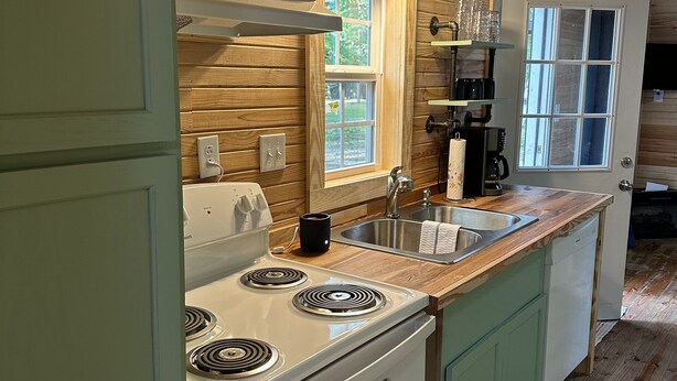 Una cocina con paredes de madera, una estufa blanca, un fregadero y una ventana con vistas al verdor.