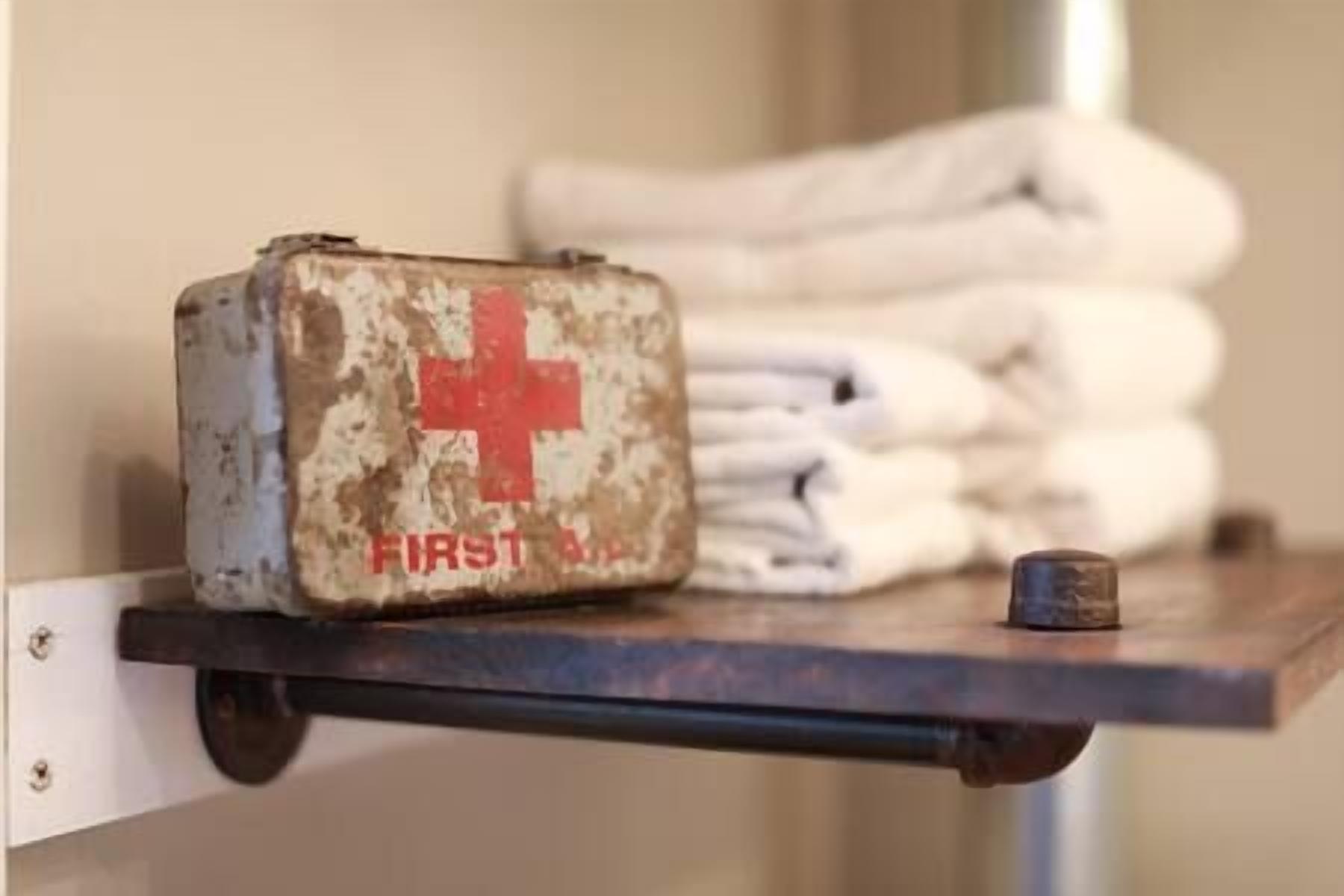 Une trousse de premiers secours est posée sur une étagère, avec des serviettes pliées en arrière-plan.