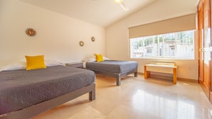 A hotel room with two beds, a bench, a ceiling fan, and a window with a view of buildings.