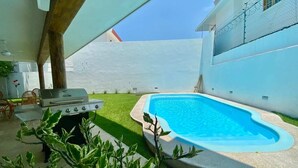 A backyard with a swimming pool, a barbecue grill, and a small patio area.