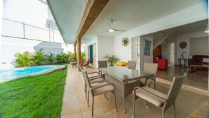 A spacious outdoor patio with a glass table and wicker chairs, a swimming pool, and a view of the adjacent living area.