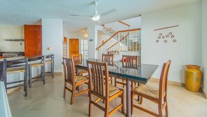 A spacious dining area with a glass-top table and wooden chairs, a kitchen with a stove, and a staircase leading to an upper level.