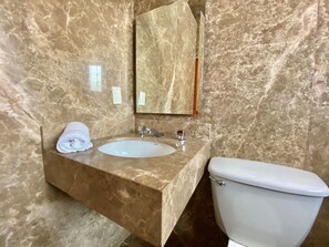 A bathroom with a marble vanity, a sink, a mirror, and a toilet.