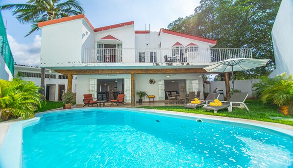 A two-story house with a swimming pool, outdoor furniture, and a covered patio area.
