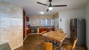 A kitchen with a wooden dining table, wicker chairs, a stainless steel refrigerator, and a ceiling fan. - Beautiful home with pool (Puerto Vallarta)
