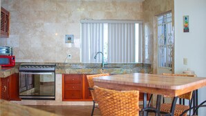 A kitchen with a stove, oven, and microwave, a dining table with chairs, and a window with blinds. - Beautiful home with pool (Puerto Vallarta)