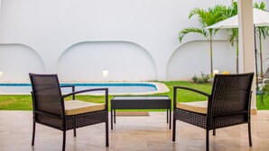 Two wicker chairs with cushions, a small table, and a pool in the background. - Beautiful home with pool (Puerto Vallarta)