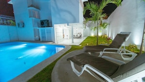 A modern outdoor pool area with lounge chairs, a small garden, and a white building with glass doors. - Spacious House with Private Pool (Puerto Vallarta)
