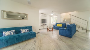 A spacious living room with two blue sofas, a coffee table, a TV, and a staircase leading to an upper floor. - Spacious House with Private Pool (Puerto Vallarta)